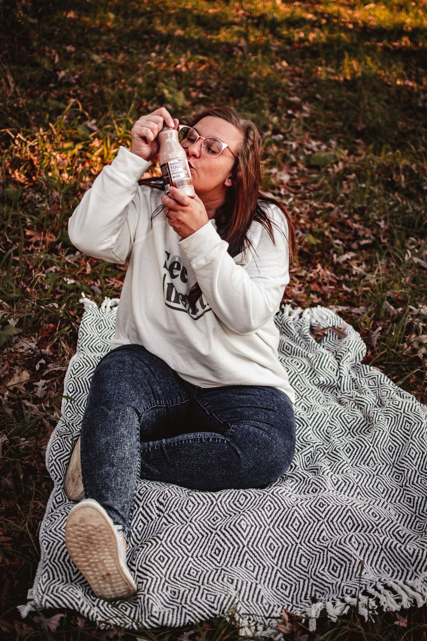 Person enjoying a beverage while relaxing on a patterned blanket in autumn woods.