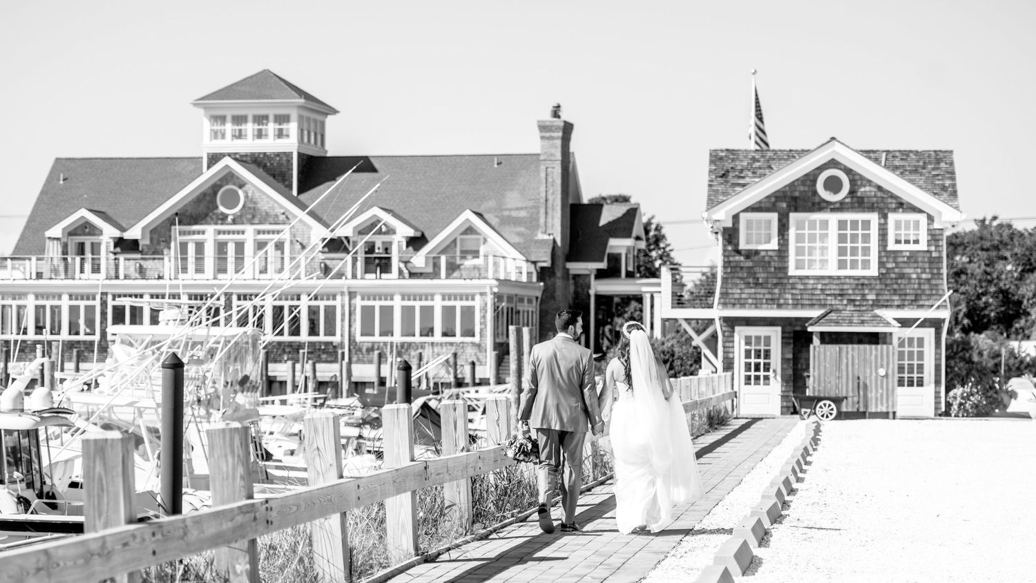 The couple walks hand in hand, at a distance, along the pier at the Peconic Bay