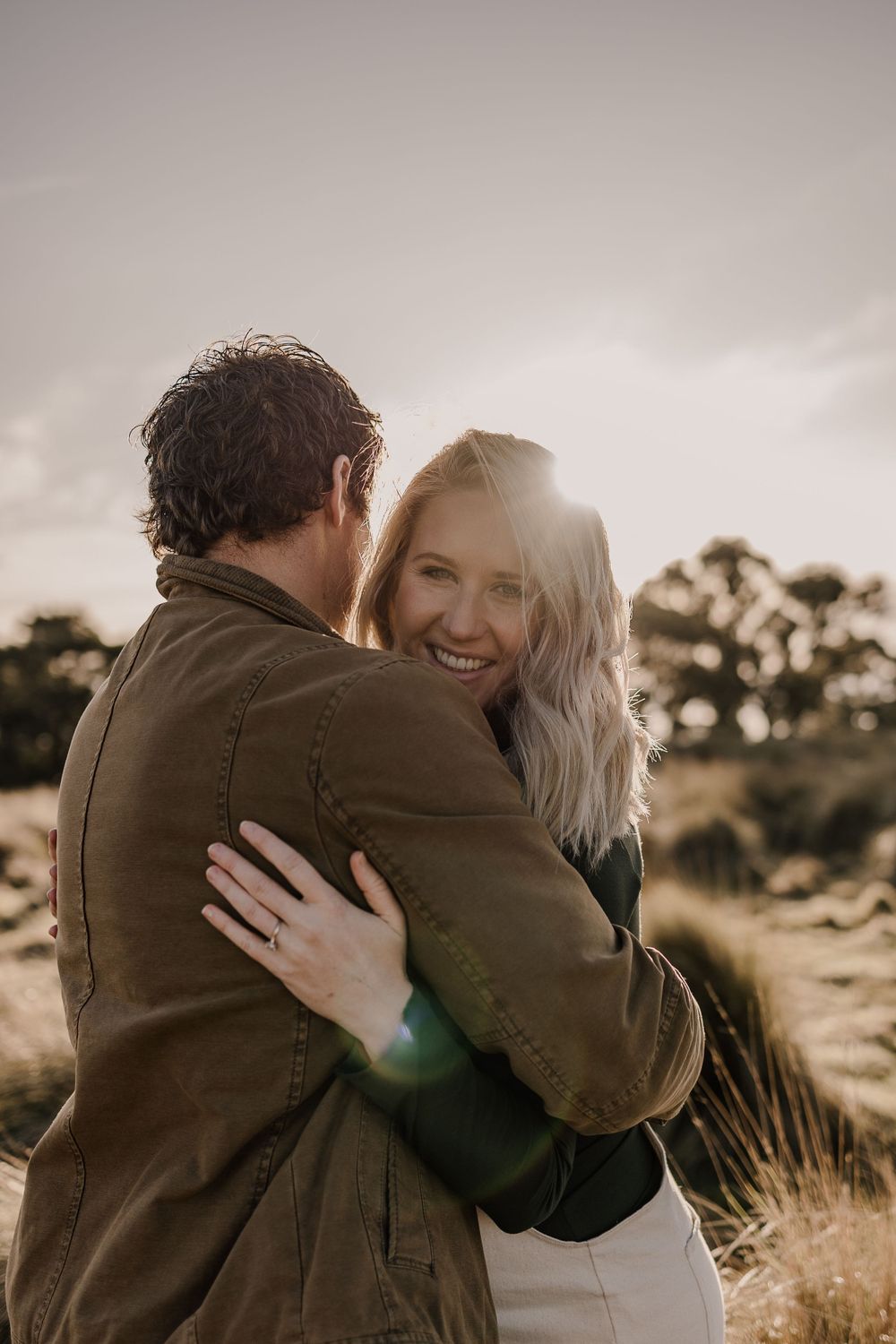 A joyful embrace captured during a sunset maternity photoshoot in a field of tall grass.