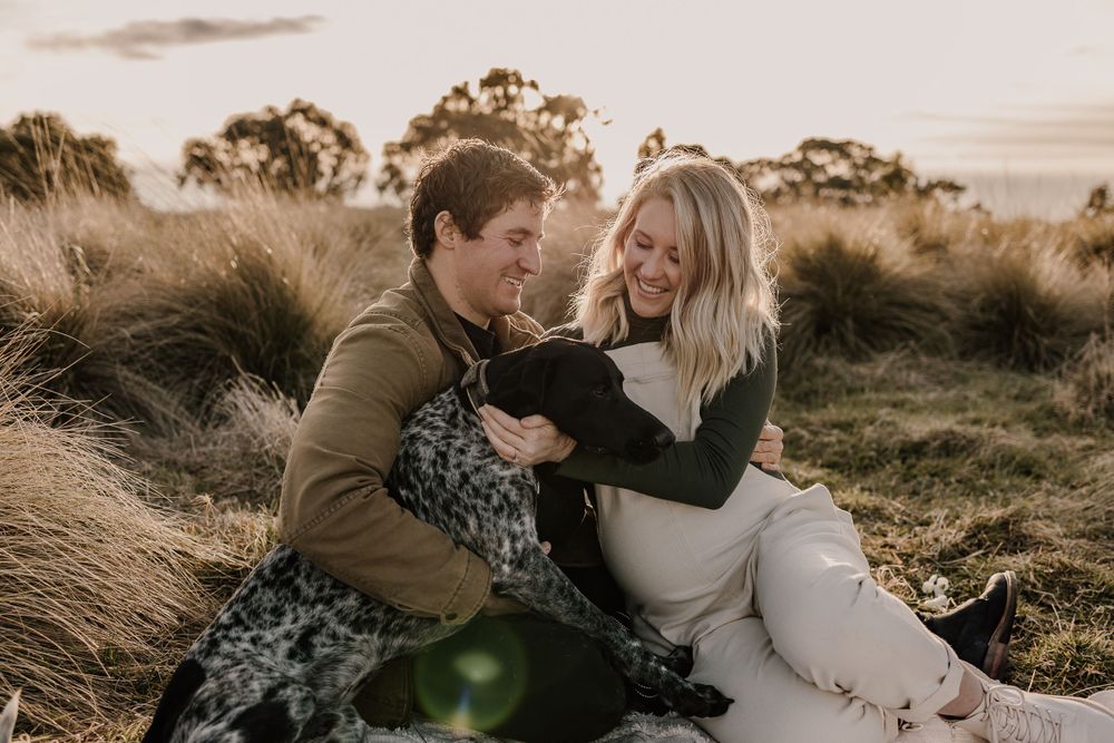 Loving couple shares laughter with their spotted dog during outdoor photo session at dusk.