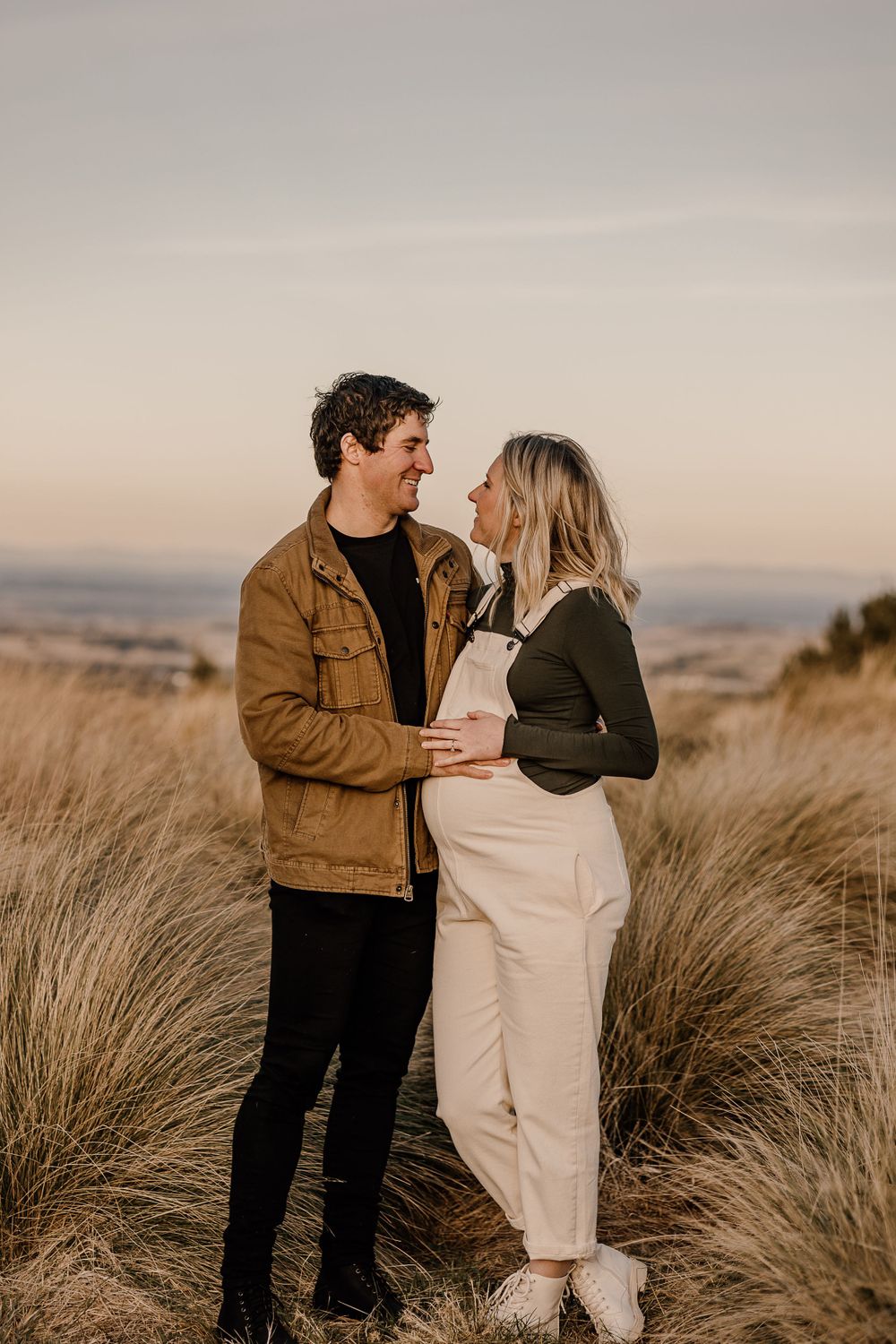 A couple shares an intimate moment among tall grass during sunset.