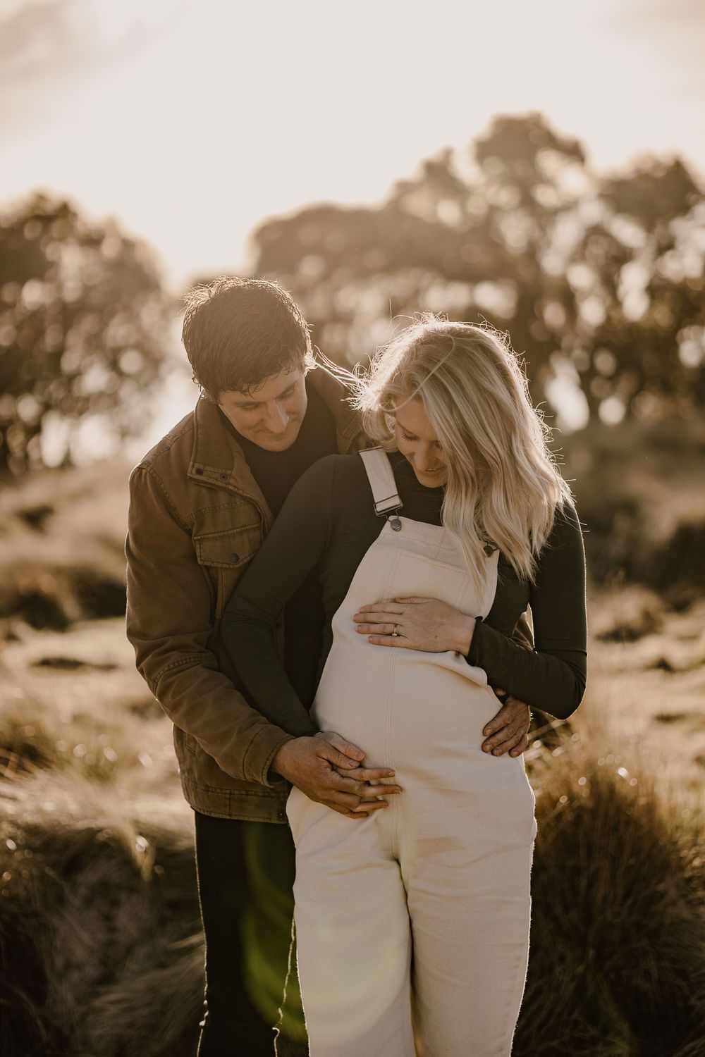 A couple shares a tender moment during their sunset maternity photoshoot in nature.