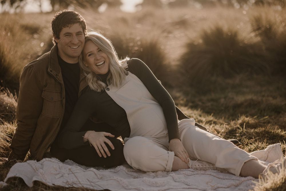 A couple snuggling on a blanket during their outdoor maternity photography session at golden hour.