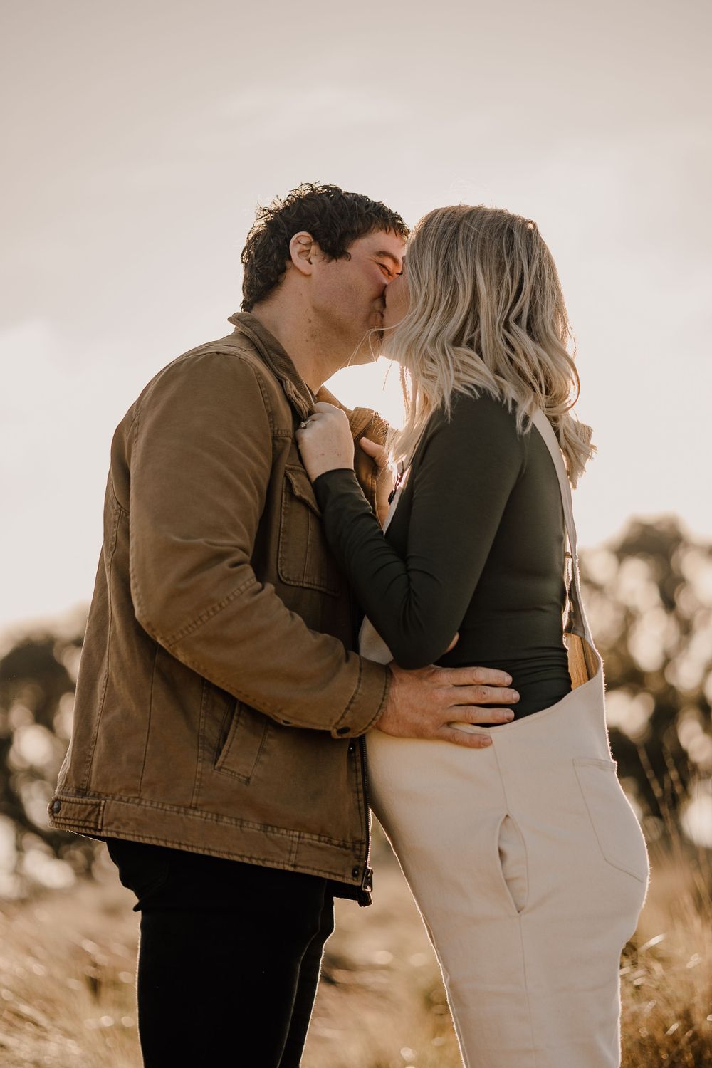 A romantic outdoor maternity photoshoot at sunset with a couple embracing in warm earth tones.
