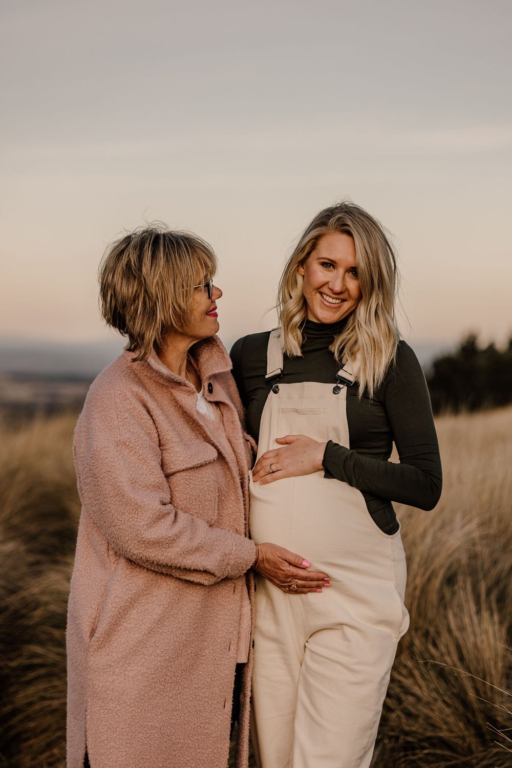 Two people share joyful expressions while standing in tall grass at sunset.