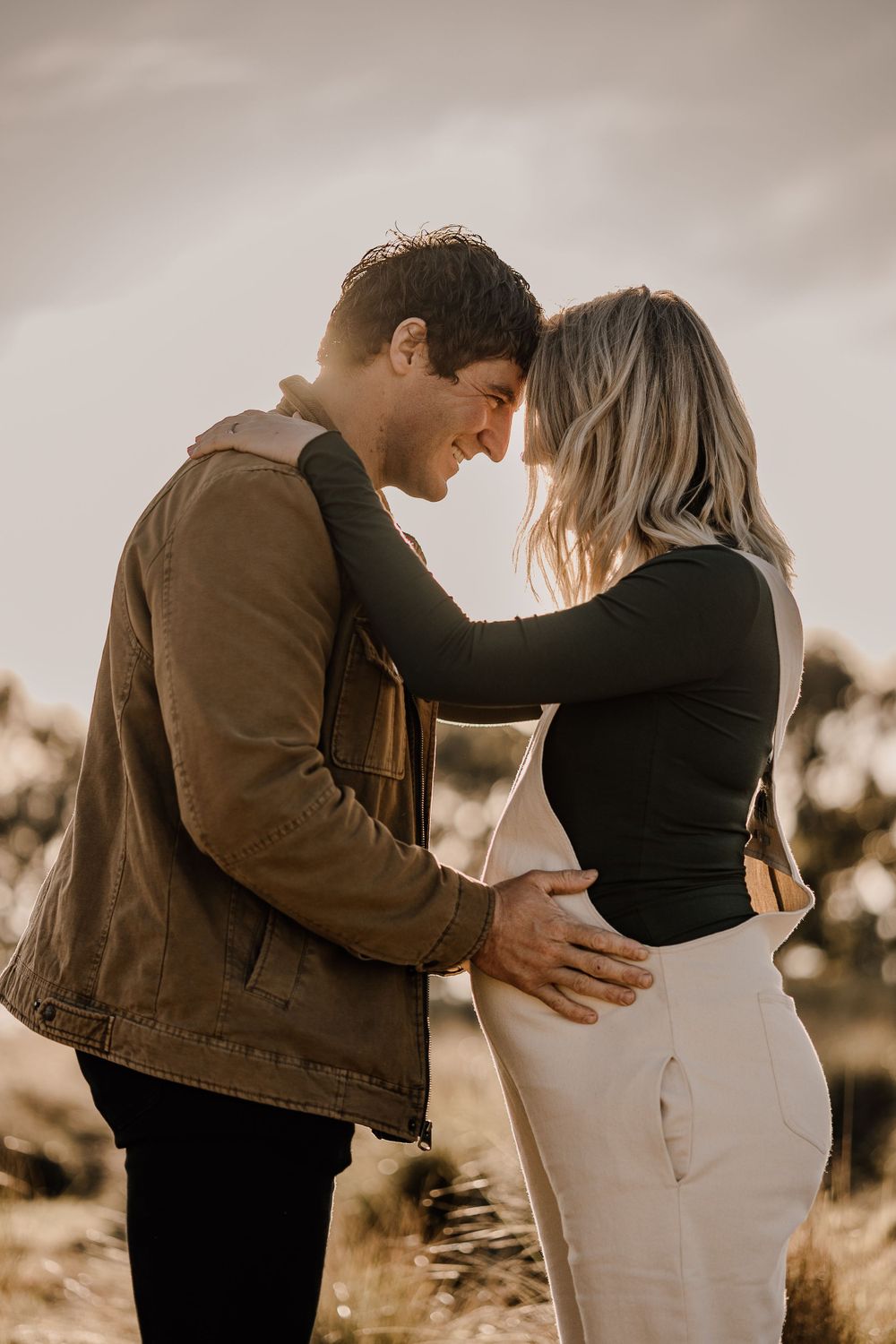 A romantic maternity photo shows a couple embracing in warm sunset light.