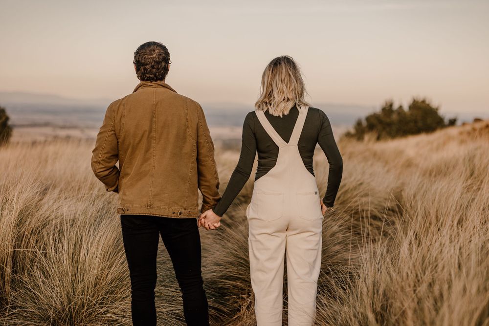 A couple in casual attire holding hands in a golden field at sunset.