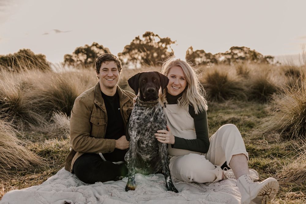 A couple and their spotted dog pose together on a blanket during an outdoor photo session.