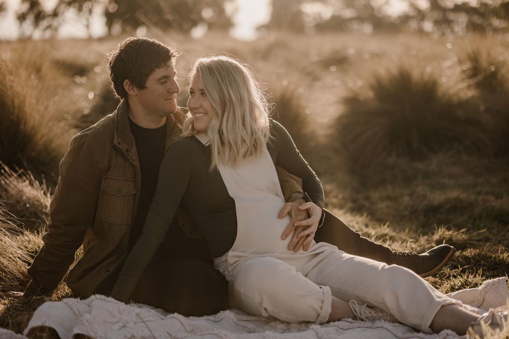 An intimate maternity photo session captures a tender moment between a couple in a natural setting.