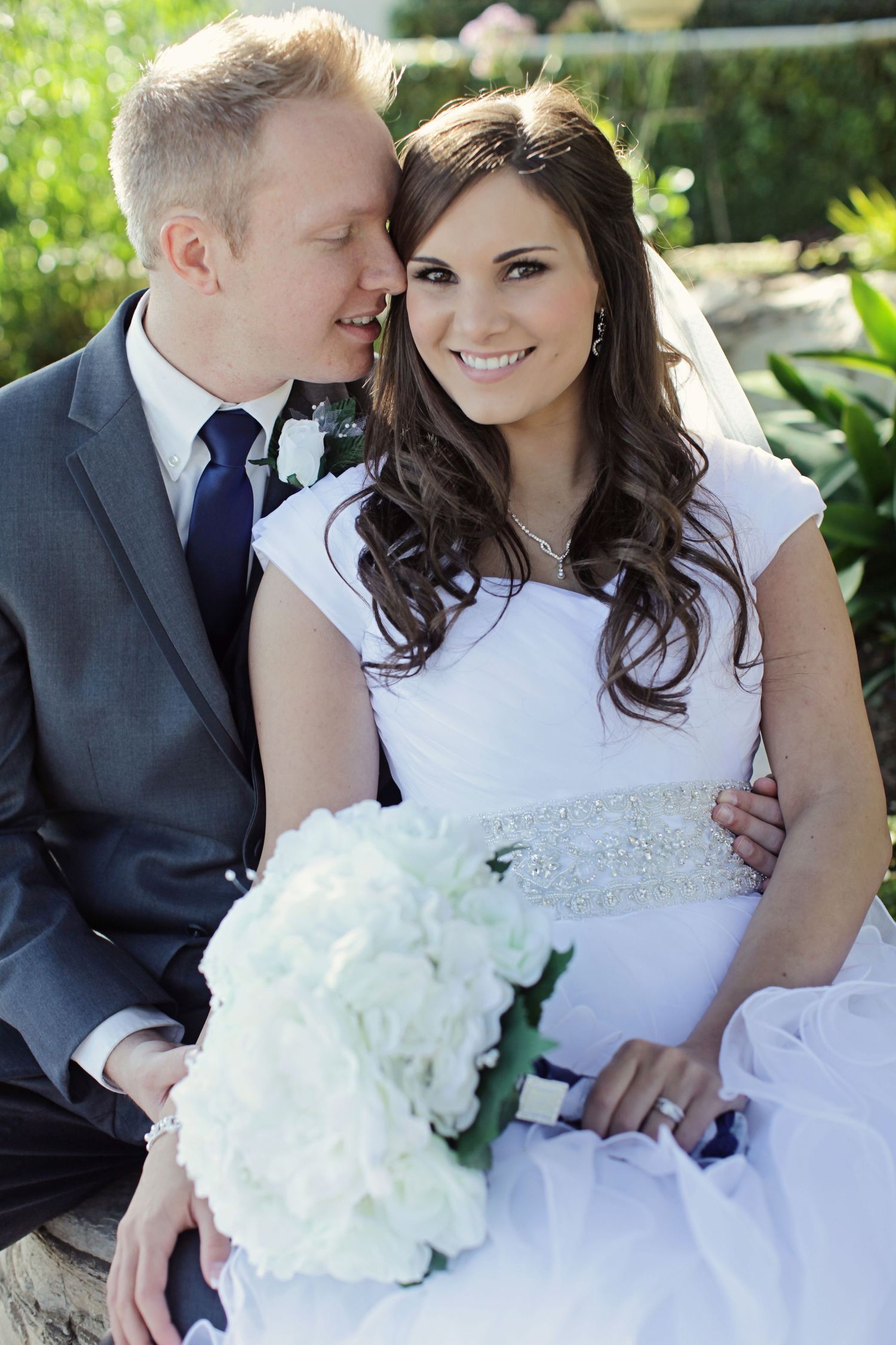 Newlywed couple with white bouquet sitting in garden setting.