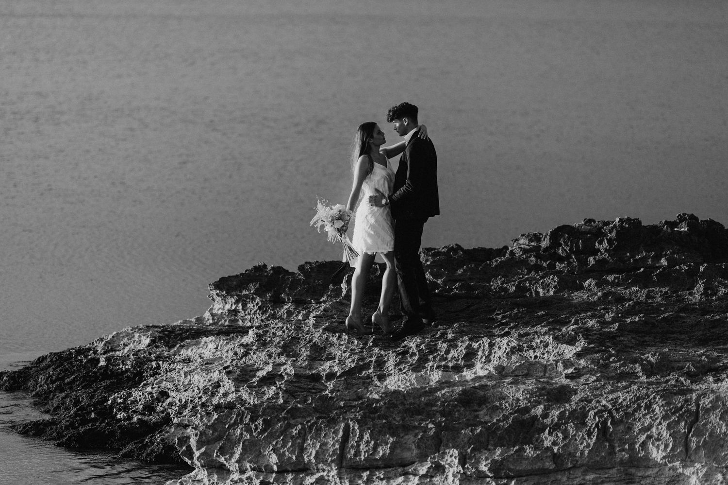 Couple posing on rocky coastal cliffs during a seaside photoshoot.