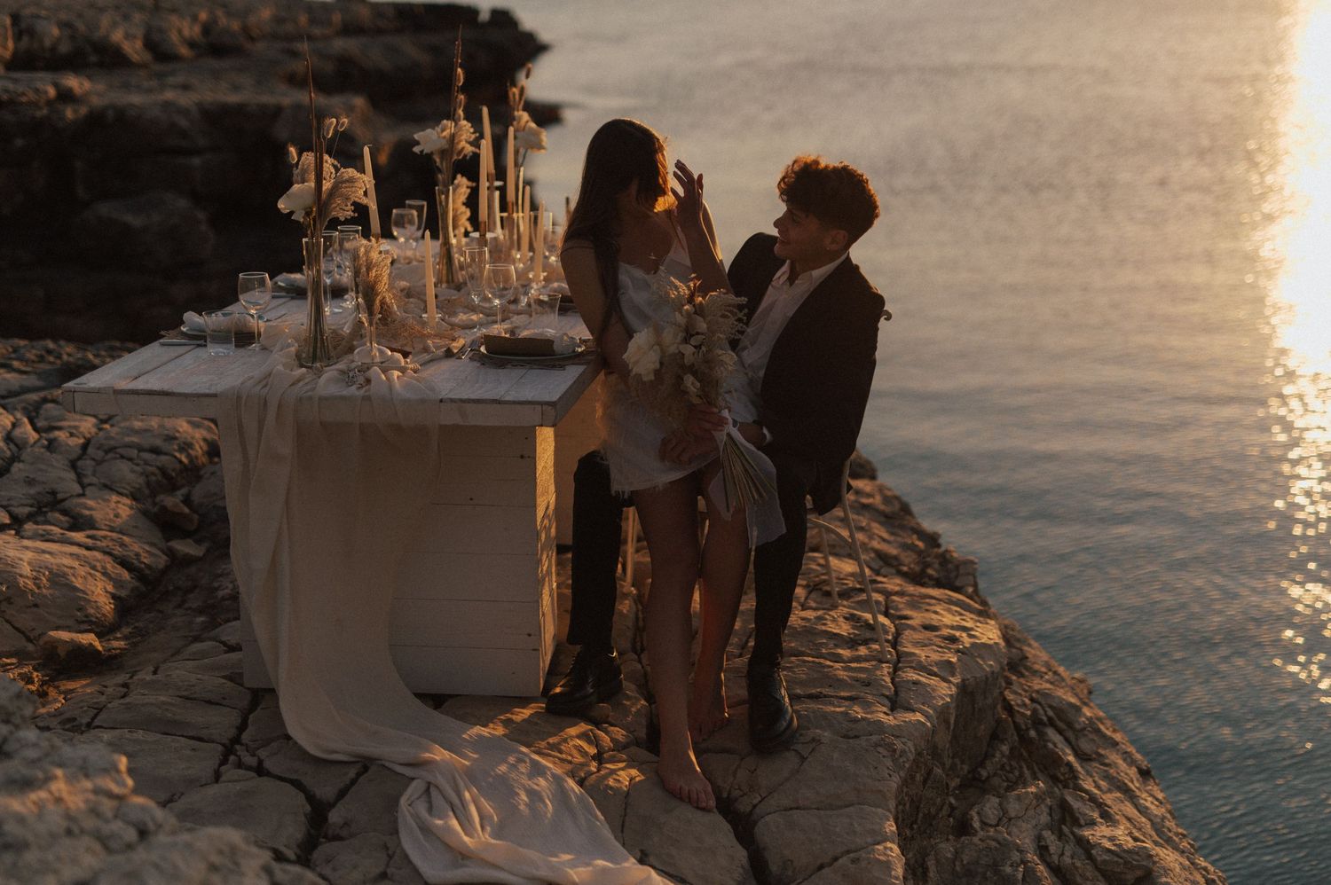 Wedding ceremony setup on rocky oceanside cliffs during golden hour.