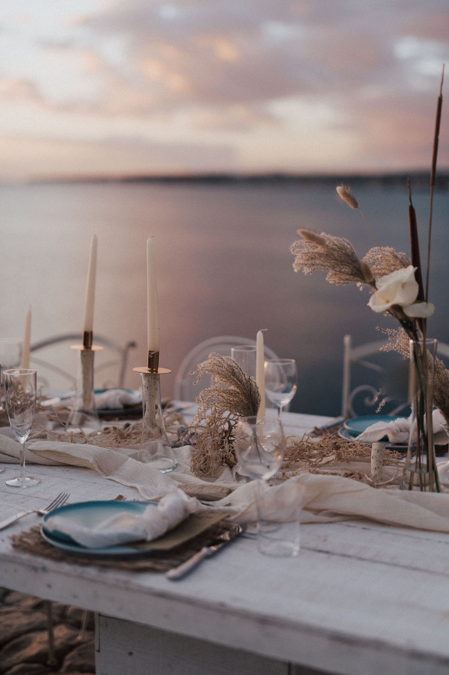 Elegant beach wedding table setting with white linens and natural decor at sunset.