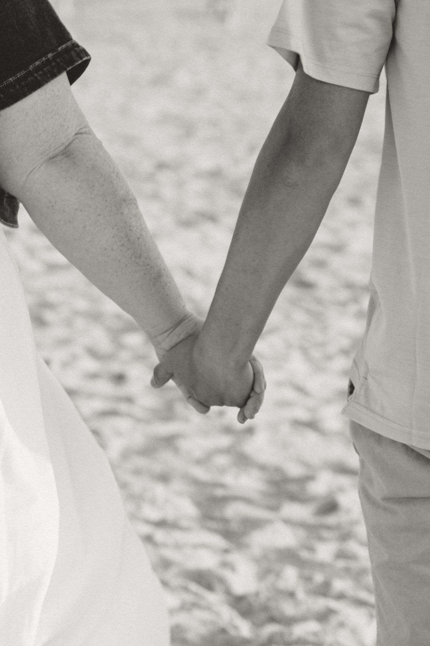 Close-up of couple's hands touching and intertwining on sandy beach.