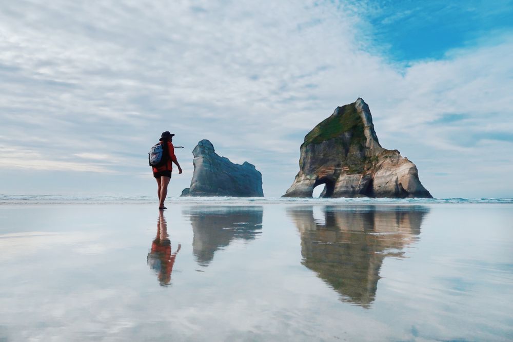 Dramatic coastal landscape with large rock formations reflected in wet sand at low tide.