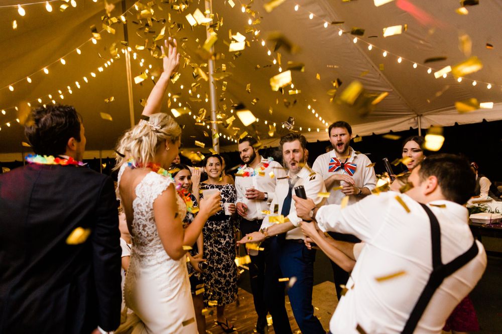Joyful wedding reception celebration with dancing and confetti under string lights.