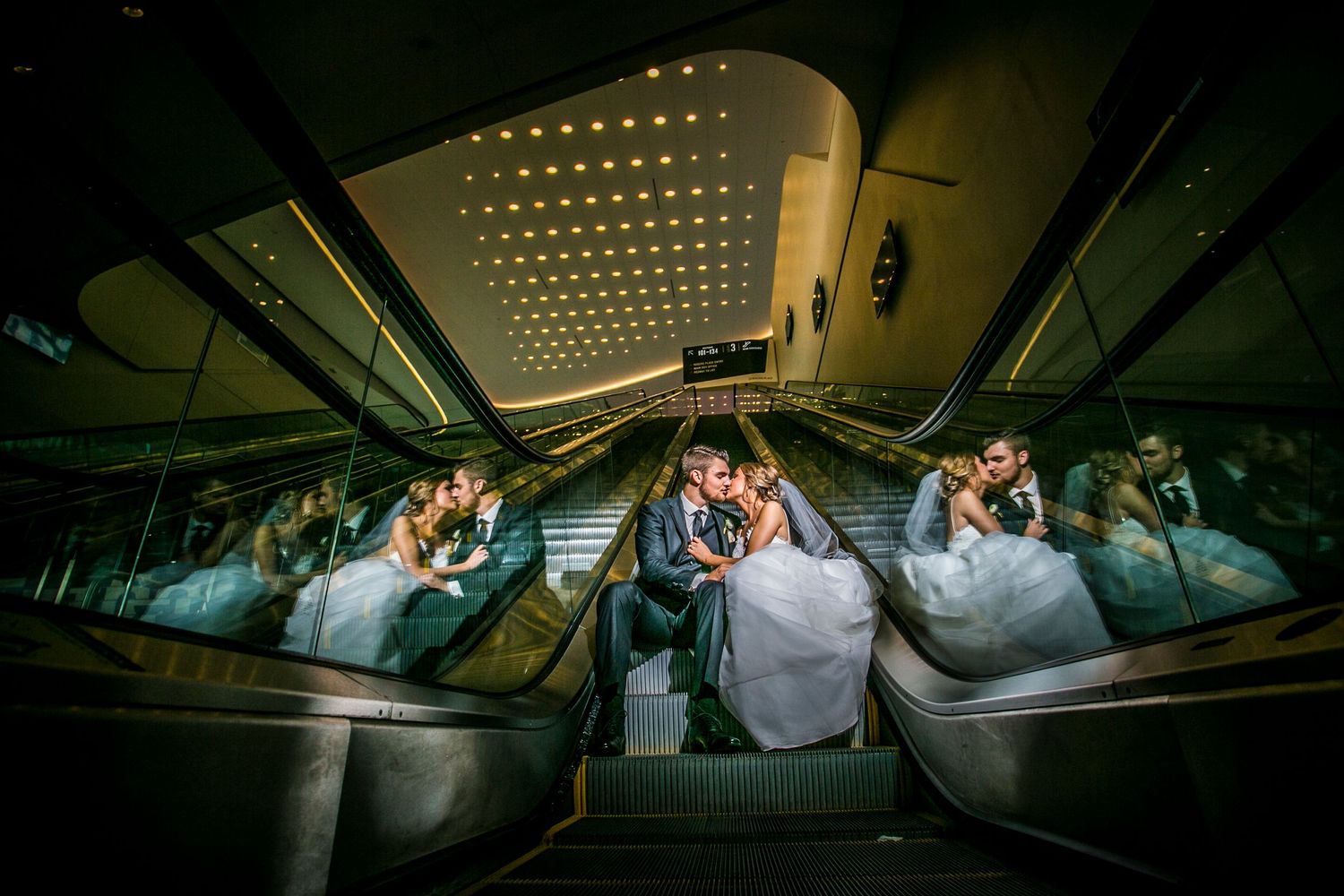 Wedding party poses creatively under dramatic architectural lighting in modern venue.