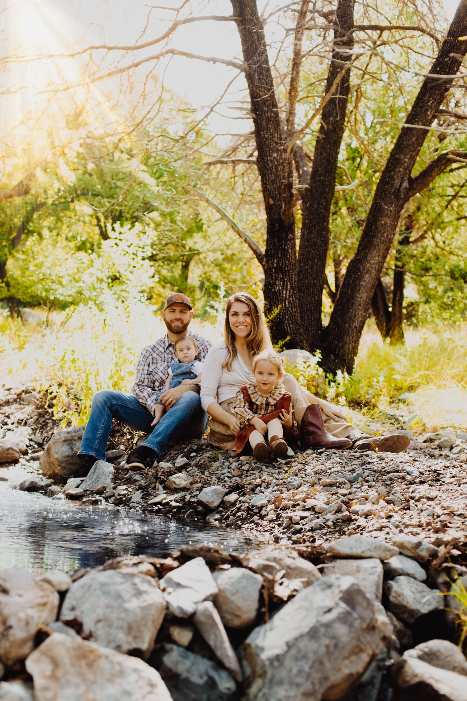 A family relaxing together by a rocky creek bed surrounded by trees.