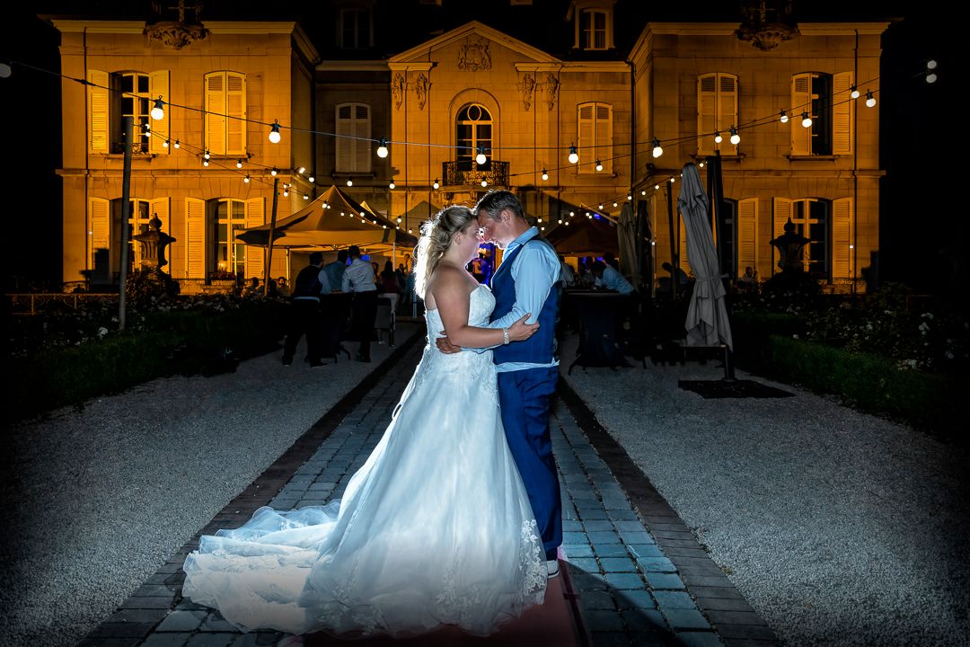 Elegant evening wedding portrait in front of a beautifully lit French-style mansion.