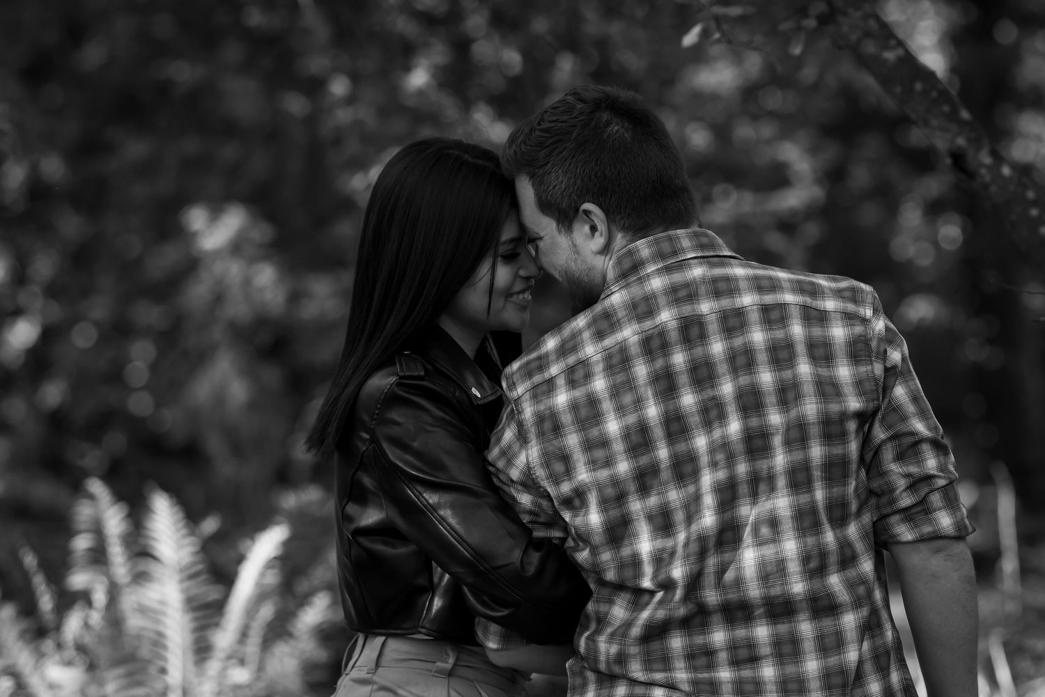 A romantic couple shares an intimate moment in a black and white outdoor setting with soft bokeh background.