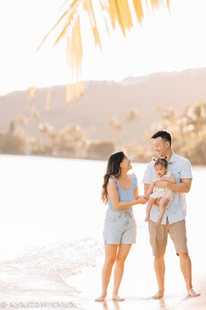 Family sharing a tender moment on a beach during golden hour with palm fronds overhead.