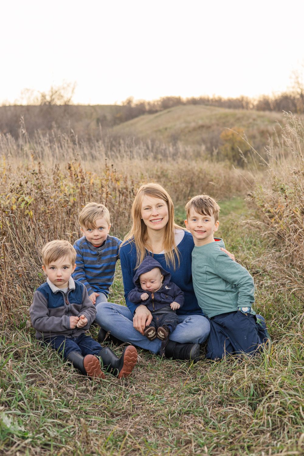 Family sitting together in a field of tall grass at sunset during an outdoor photo session.