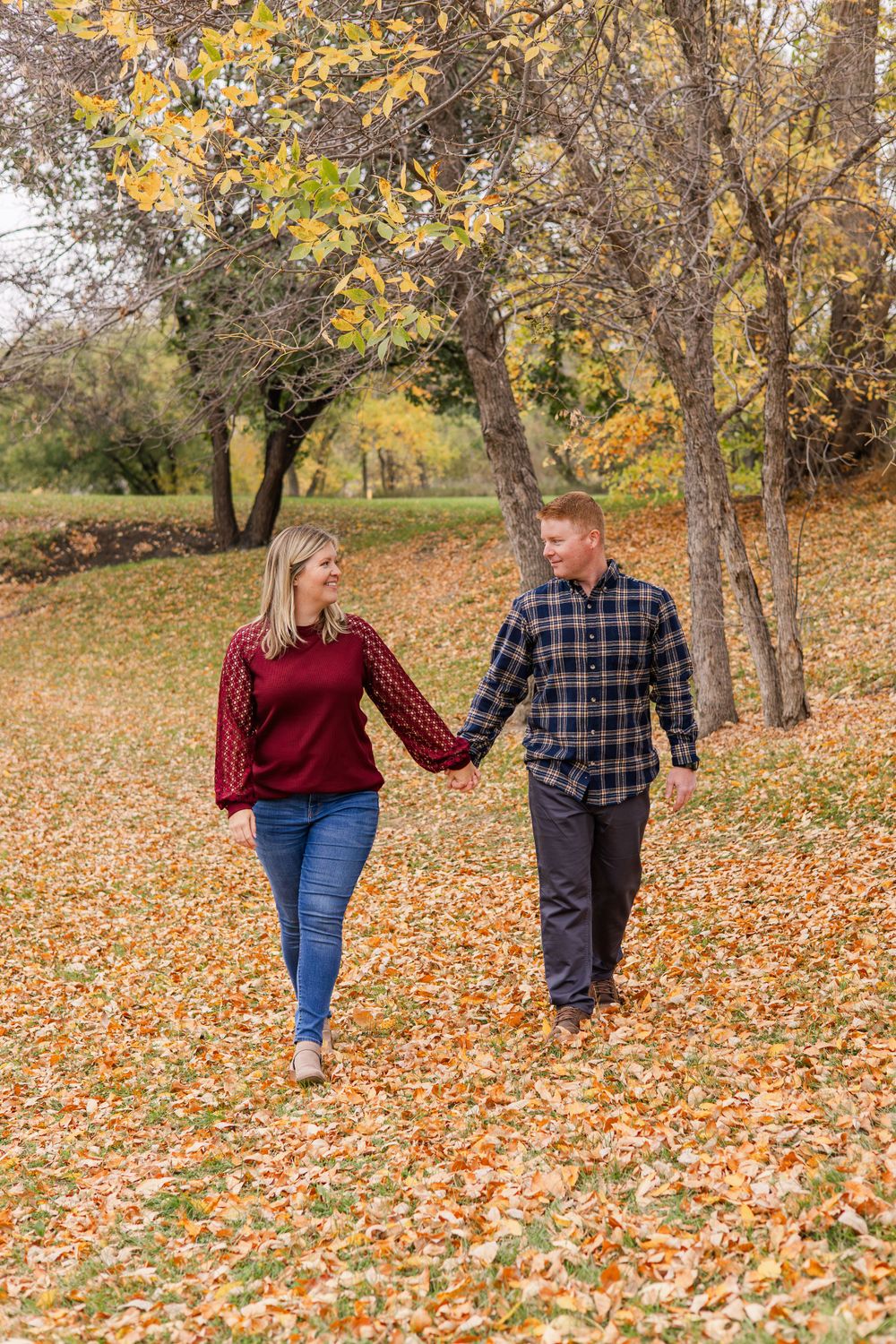 Couple walking hand in hand through fallen autumn leaves in a park.