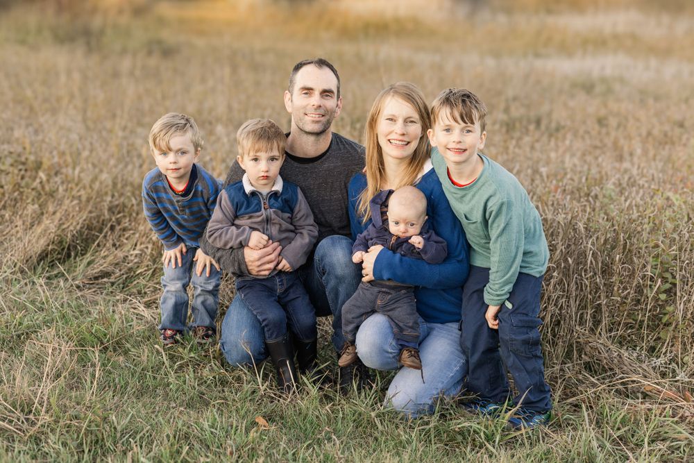 Family sitting together in tall grass field during golden hour.