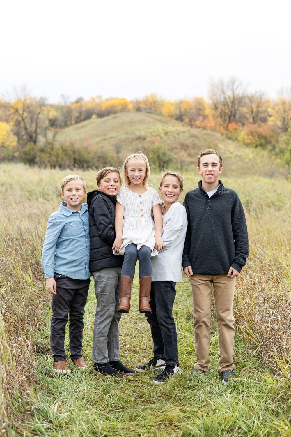 Family of five posing together on grassy hillside during fall season.