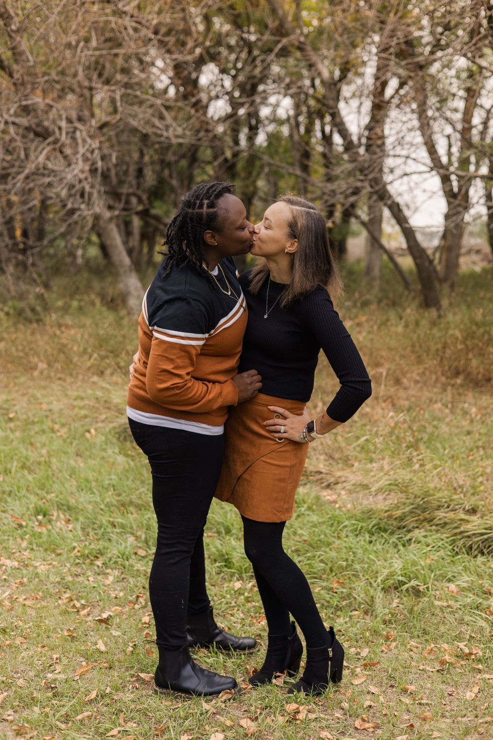 Two people sharing an affectionate moment in coordinated brown and black outfits outdoors.