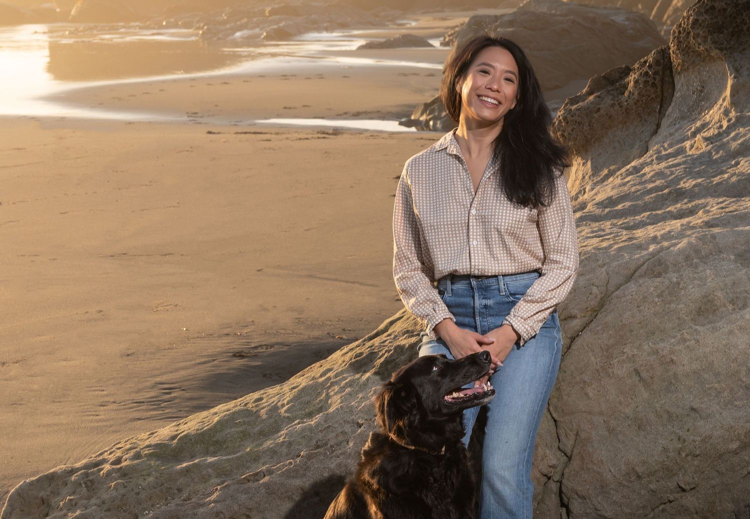 Person sitting with dog on beach cliff during golden hour sunset. At The Sea Ranch Lodge in Northern California.