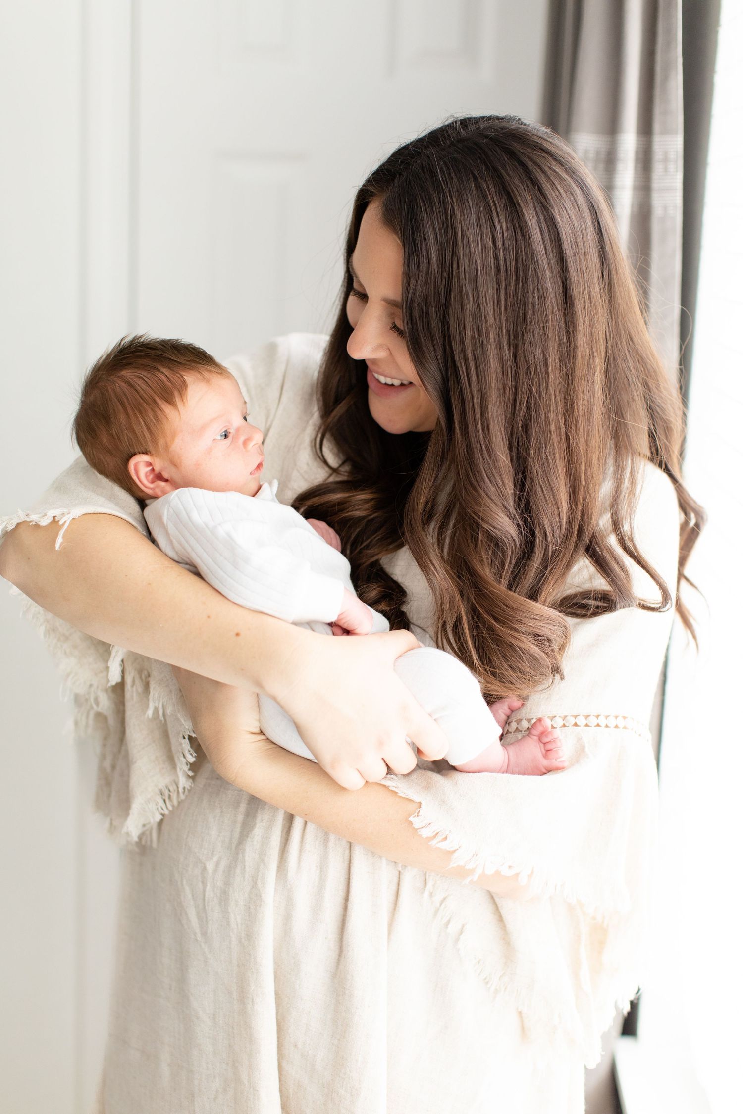 Loving interaction between parent and baby in white clothing against neutral background.