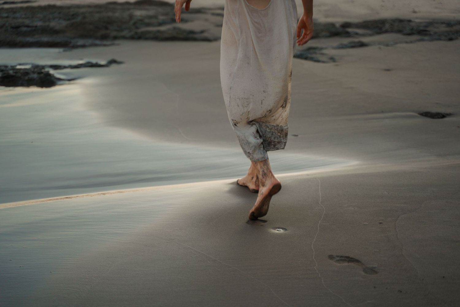 Barefoot steps leaving footprints on wet sand at the beach during sunset.