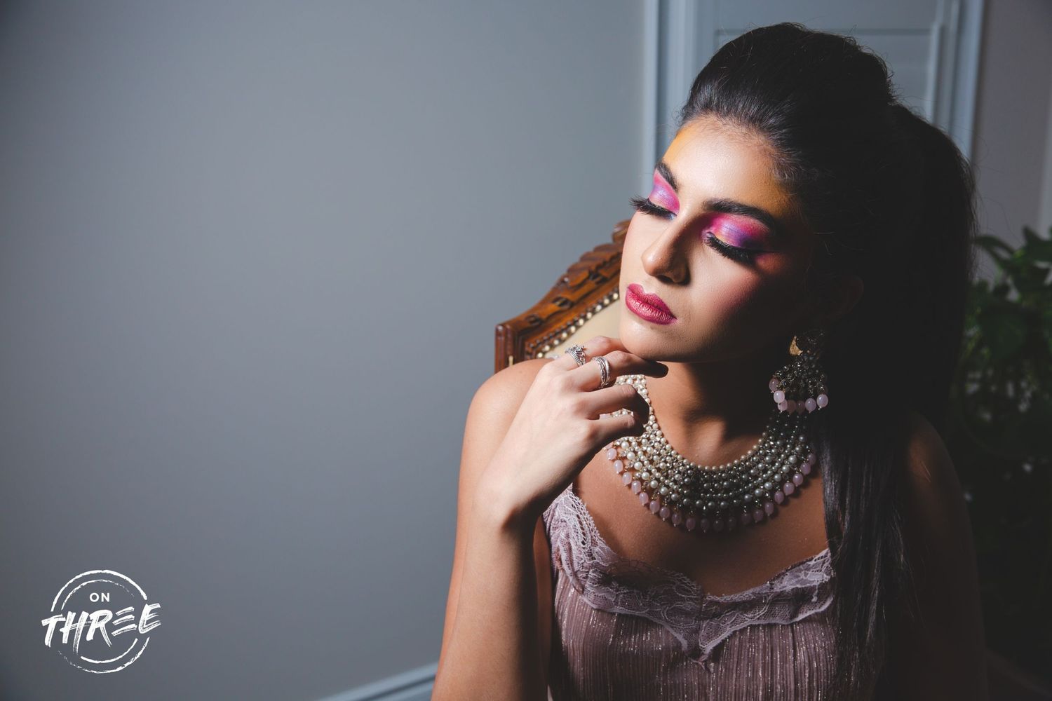 Glamorous beauty portrait featuring vibrant pink eyeshadow, layered silver necklaces, and dramatic lighting effects.