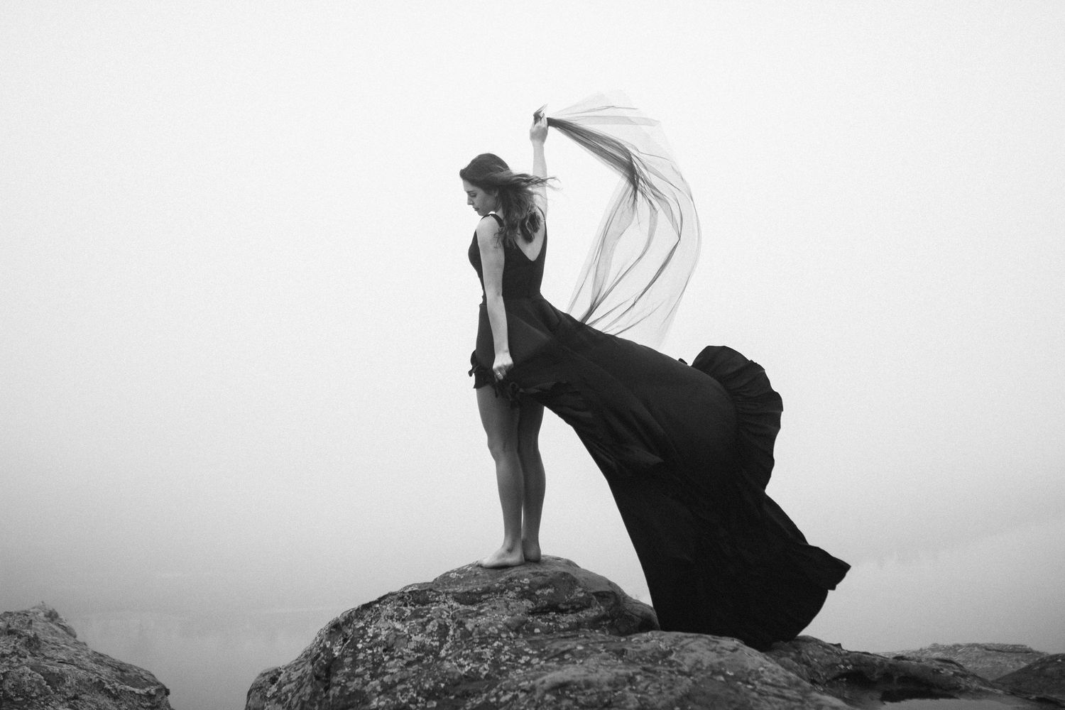 highschool senior on a fog filled mountain top in a long black ruffled dress that's being blown in the wind