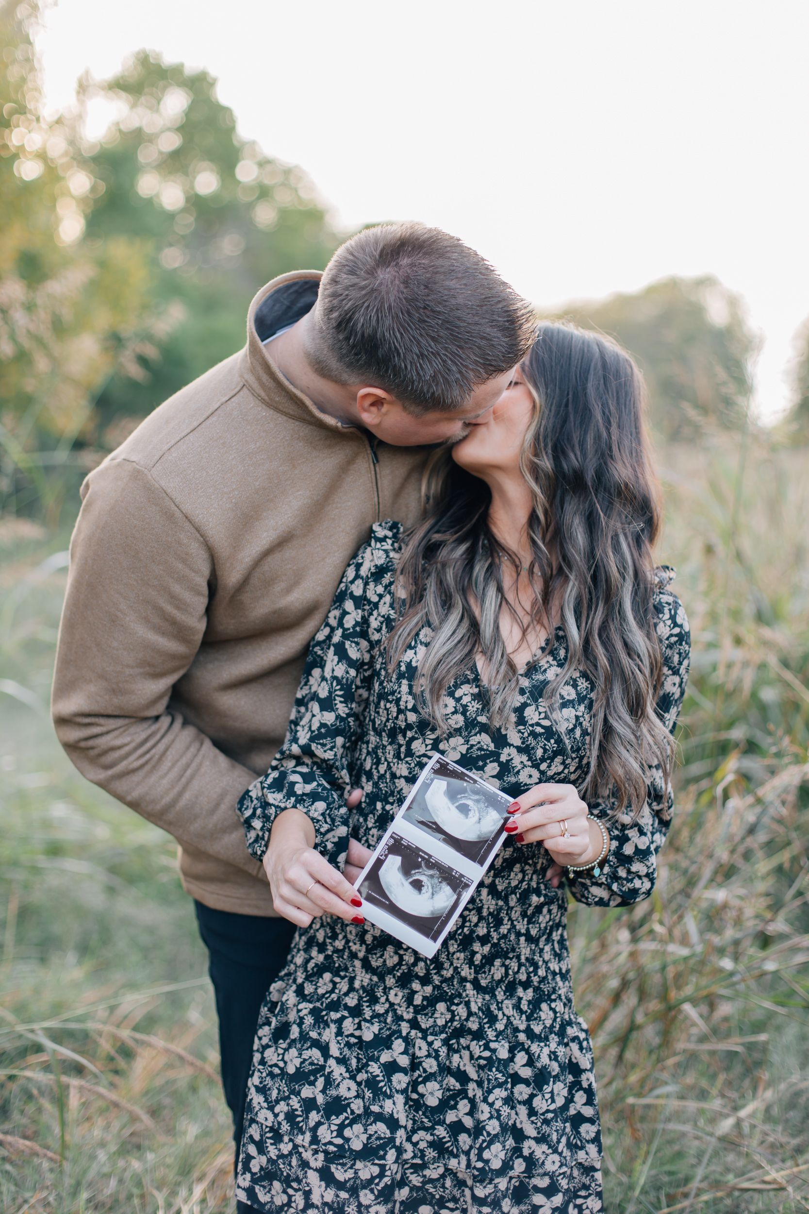 Romantic couple sharing intimate moment in field while holding ultrasound photo.