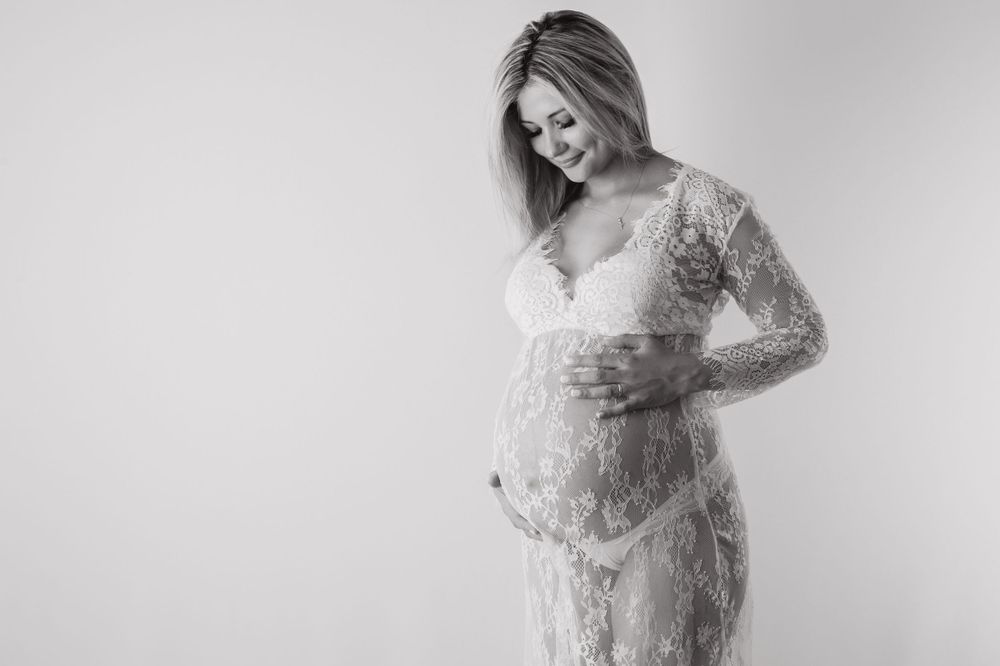 Black and white maternity photo of pregnant woman in lace dress cradling her baby bump.