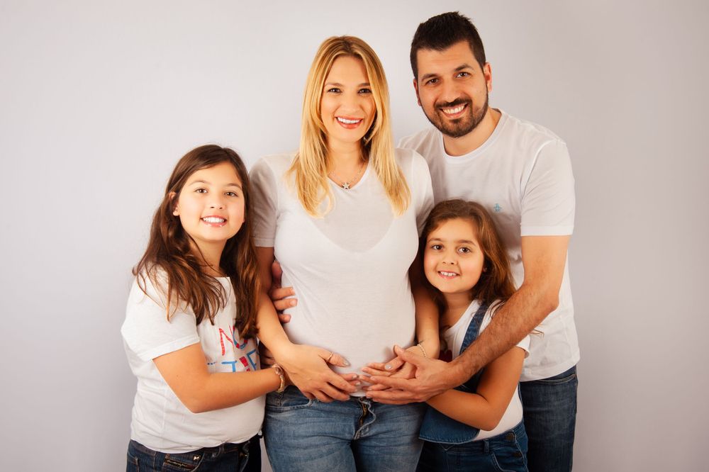 Happy family maternity photo with pregnant mother, father, and two daughters in white shirts.