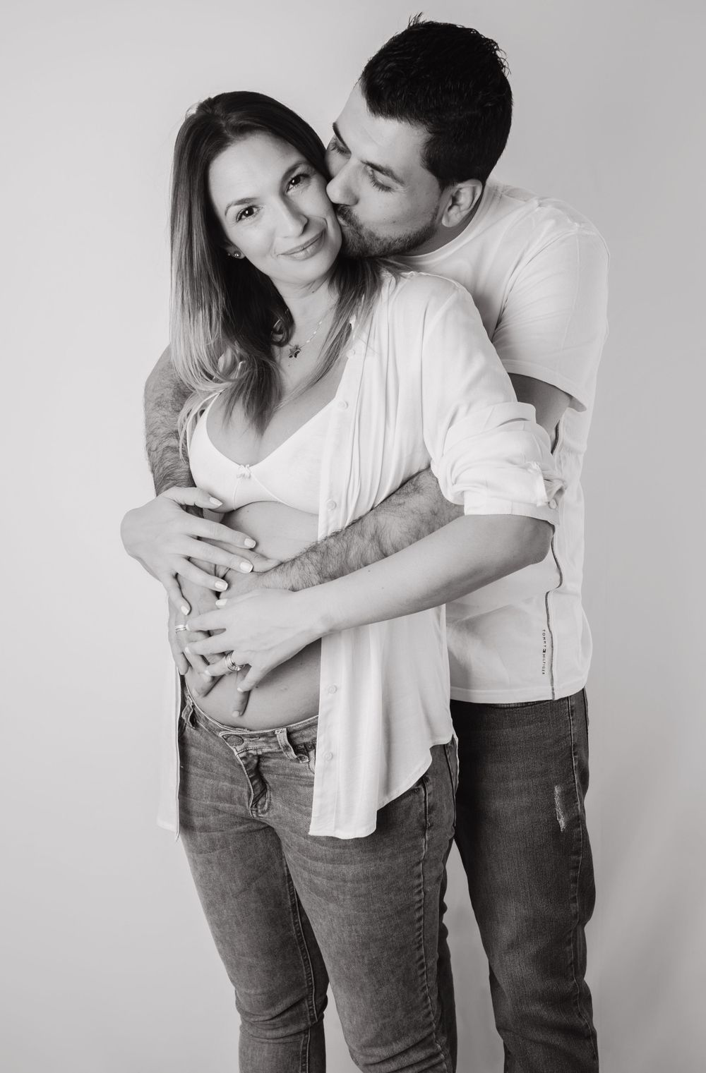 Black and white maternity photo of a couple embracing, man kissing woman's head while holding her baby bump.