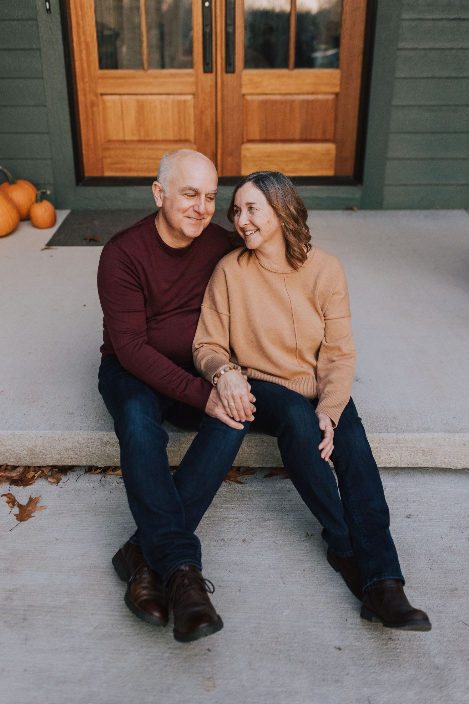 middle aged couple sitting on front porch steps smiling at one another while holding hands