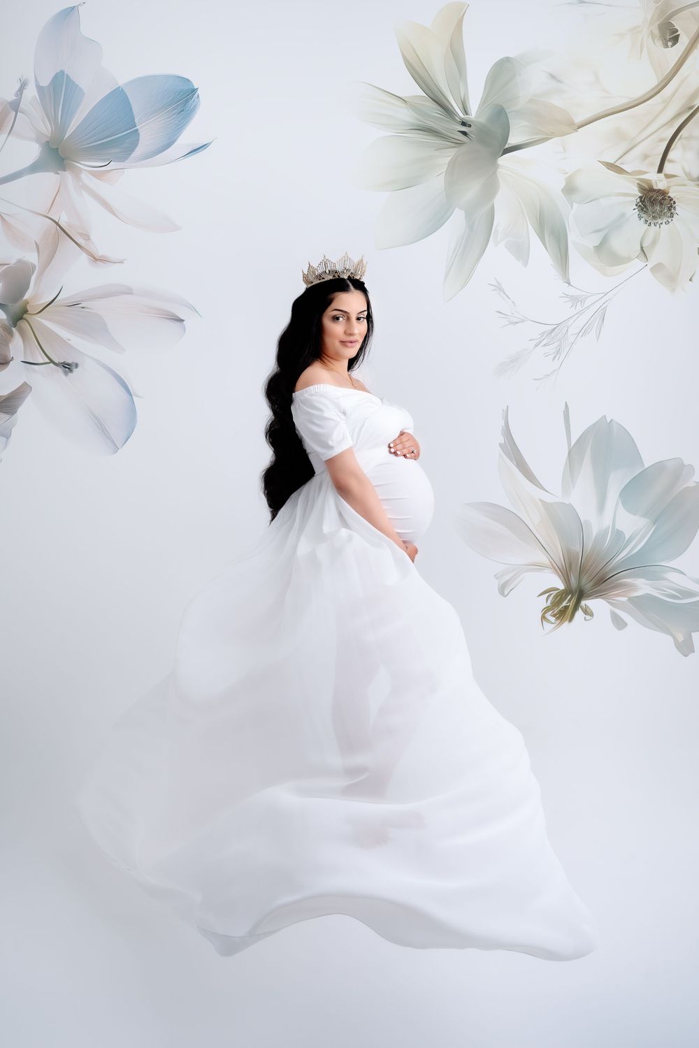 Ethereal maternity photoshoot with flowing white dress and delicate floral overlays in soft pastel tones.