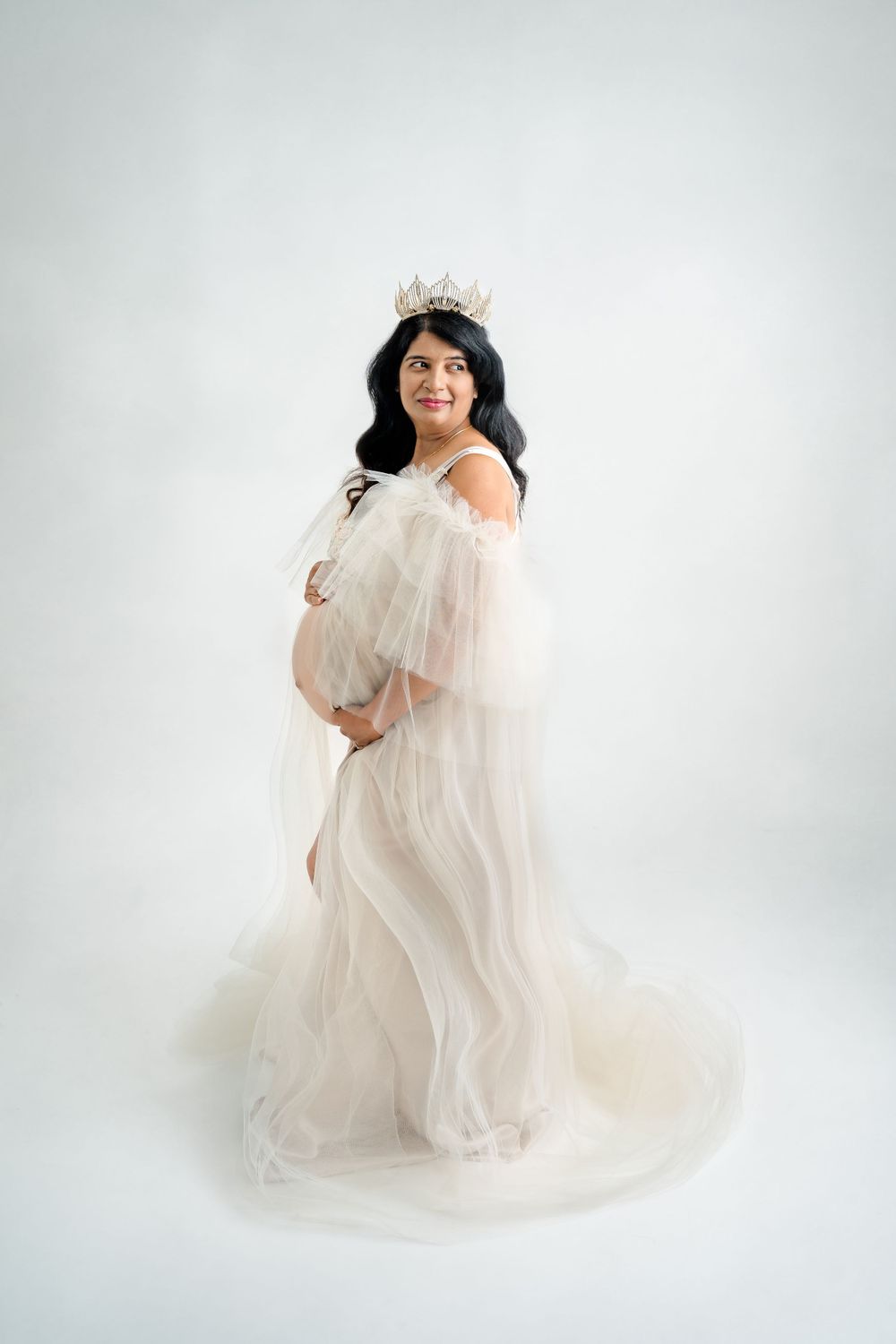 Ethereal maternity portrait with flowing sheer fabric in studio setting.
