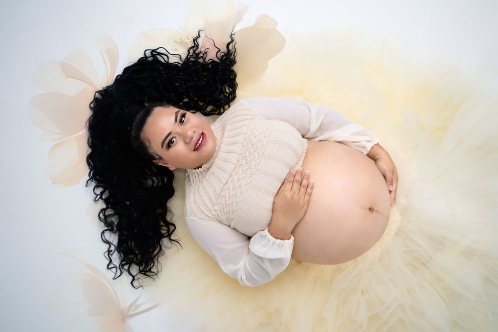 Elegant maternity pose on cream background wearing lace top and flowing tulle skirt.