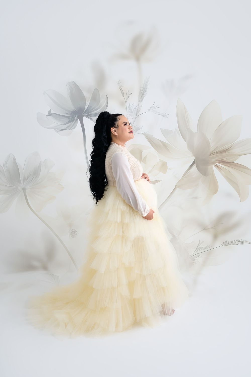 Whimsical maternity portrait with cream tulle skirt and floating flower elements.