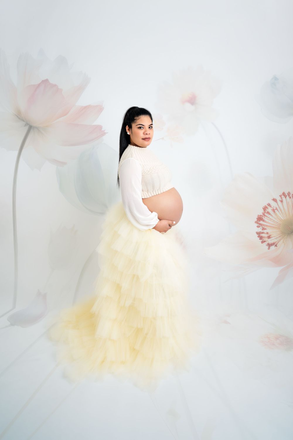 Romantic maternity photo with yellow tulle skirt and delicate floral background.