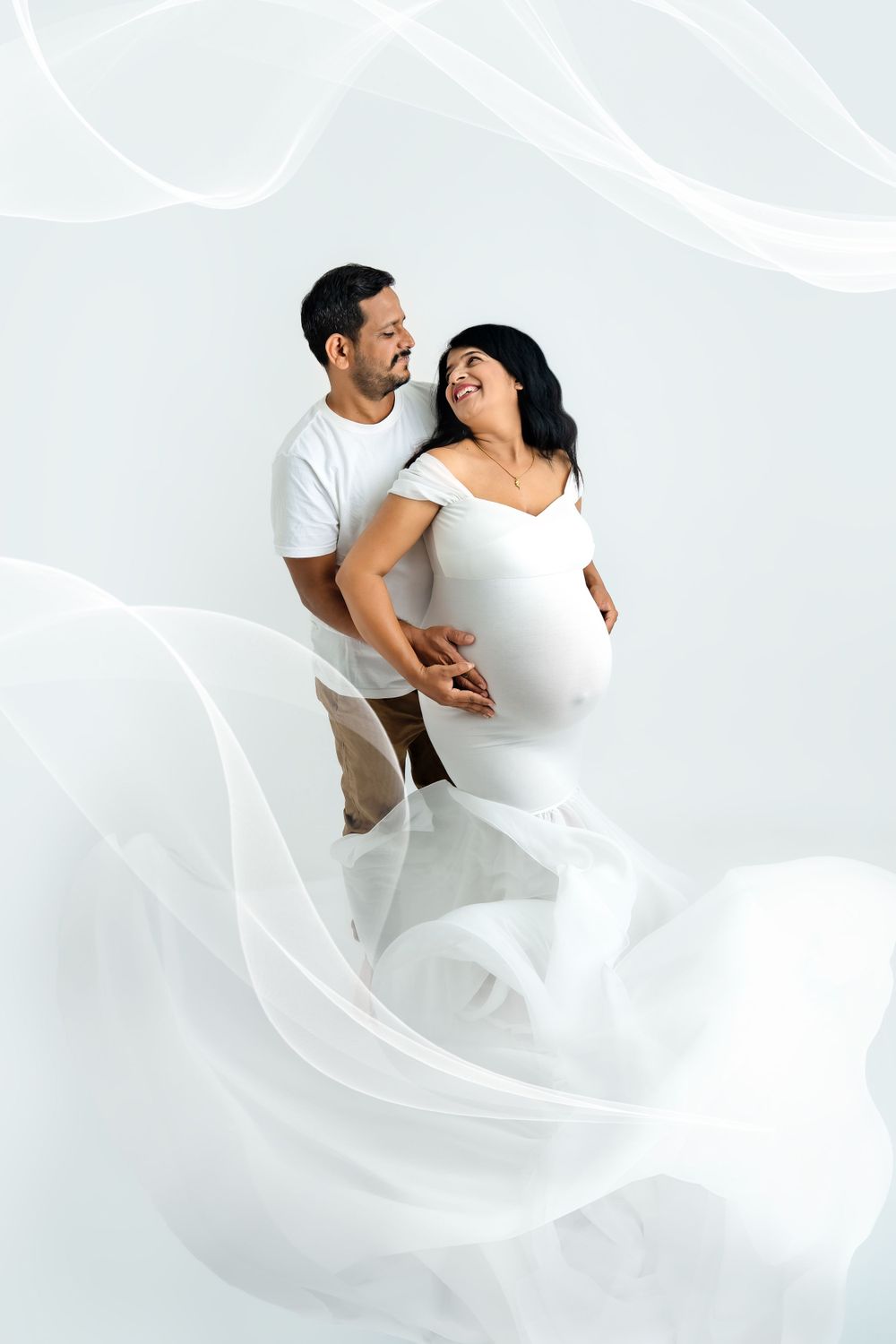 Couple in white embracing during romantic maternity photoshoot.