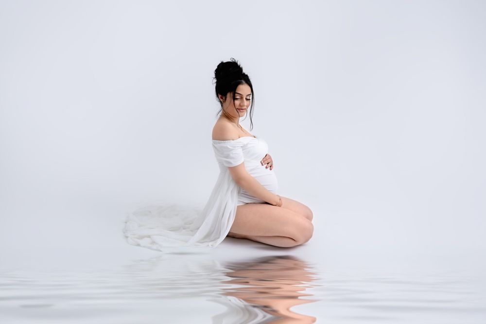 Artistic maternity portrait with sheer white fabric in minimalist studio setting.