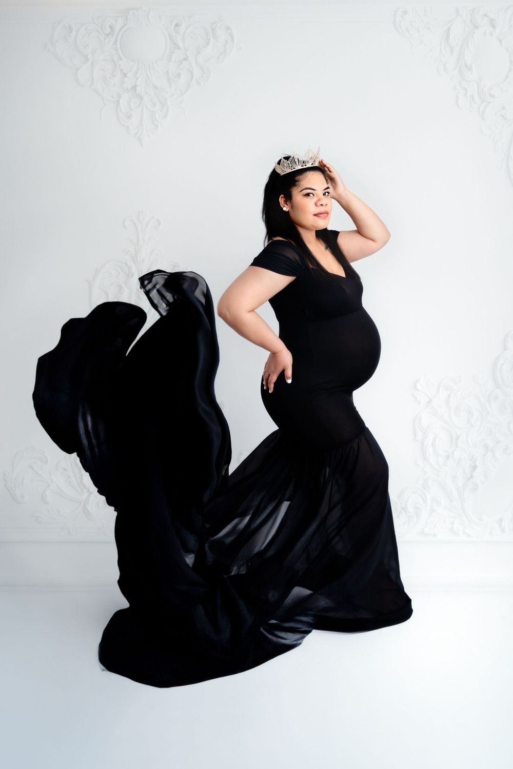 Dramatic maternity photos in flowing black gown against white studio backdrop.