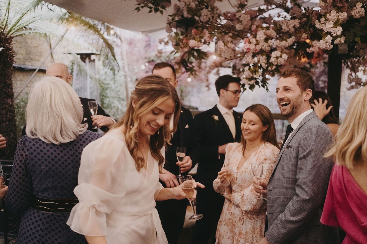 Elegant wedding reception with guests enjoying drinks under pink floral decorations.