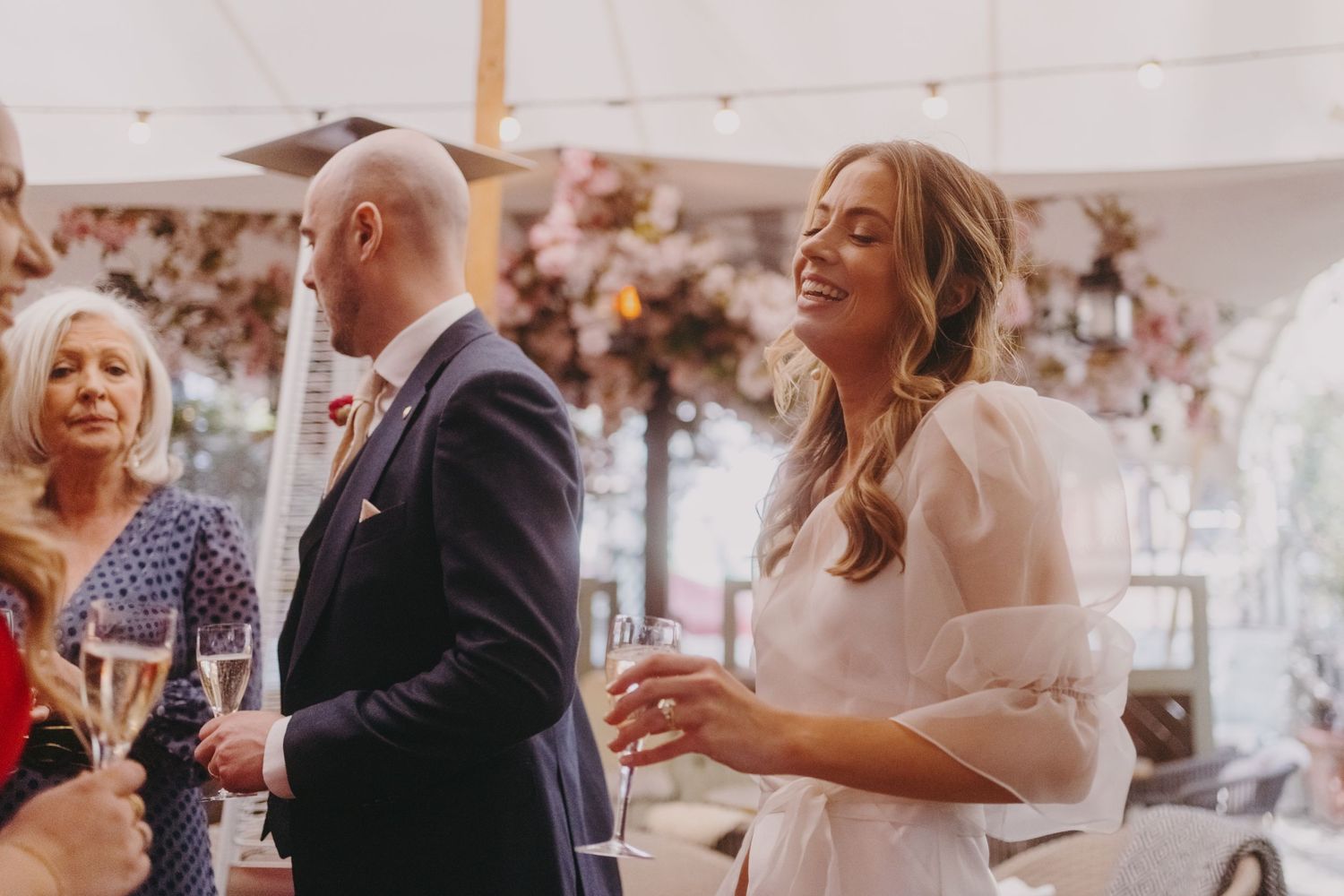 Wedding guests enjoying drinks and conversation under a decorated tent.
